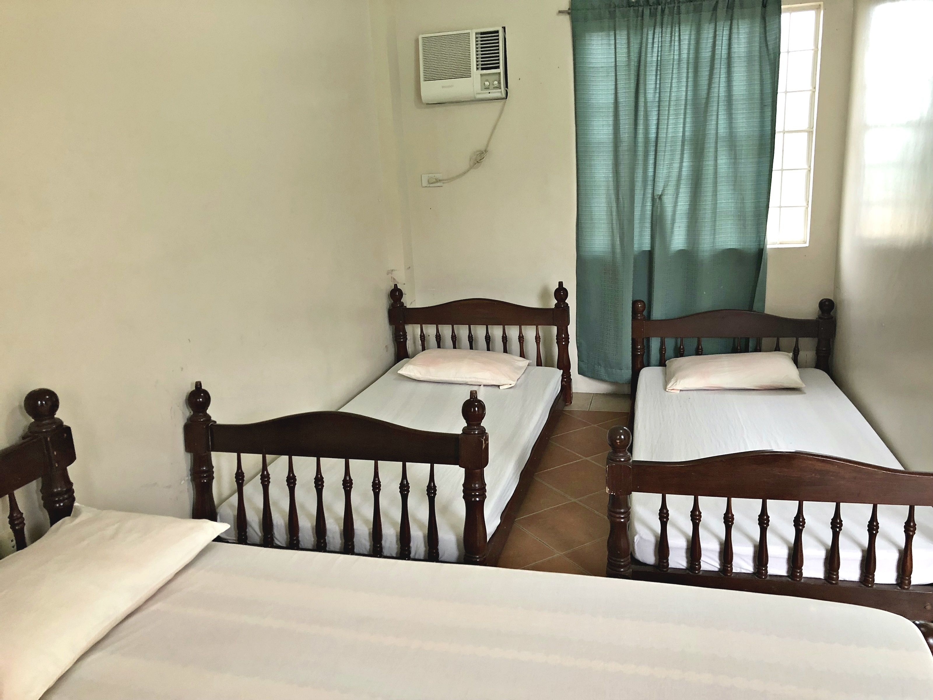 A room with two wooden beds, a window with curtains, and a wall-mounted air conditioner.