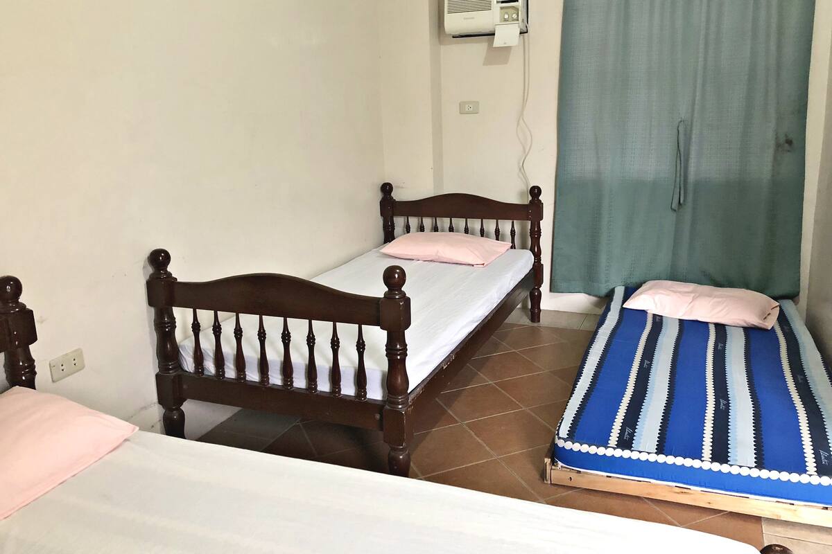 A small room with two wooden beds, a green curtain, and an air conditioning unit on the wall.