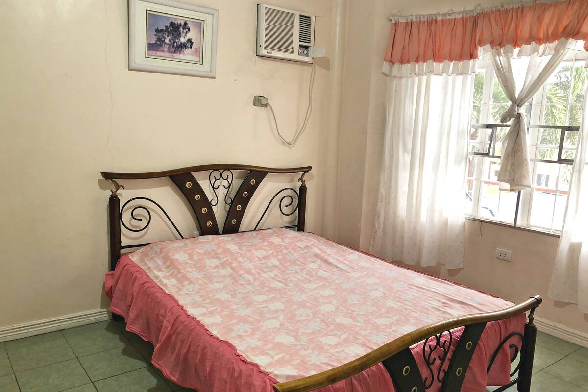 A bedroom with a bed, a picture on the wall, an air conditioner, and a window with curtains.
