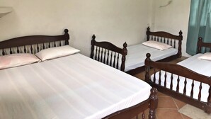 Una habitación con tres camas de madera, ropa de cama blanca, aire acondicionado de pared y una ventana con cortina.