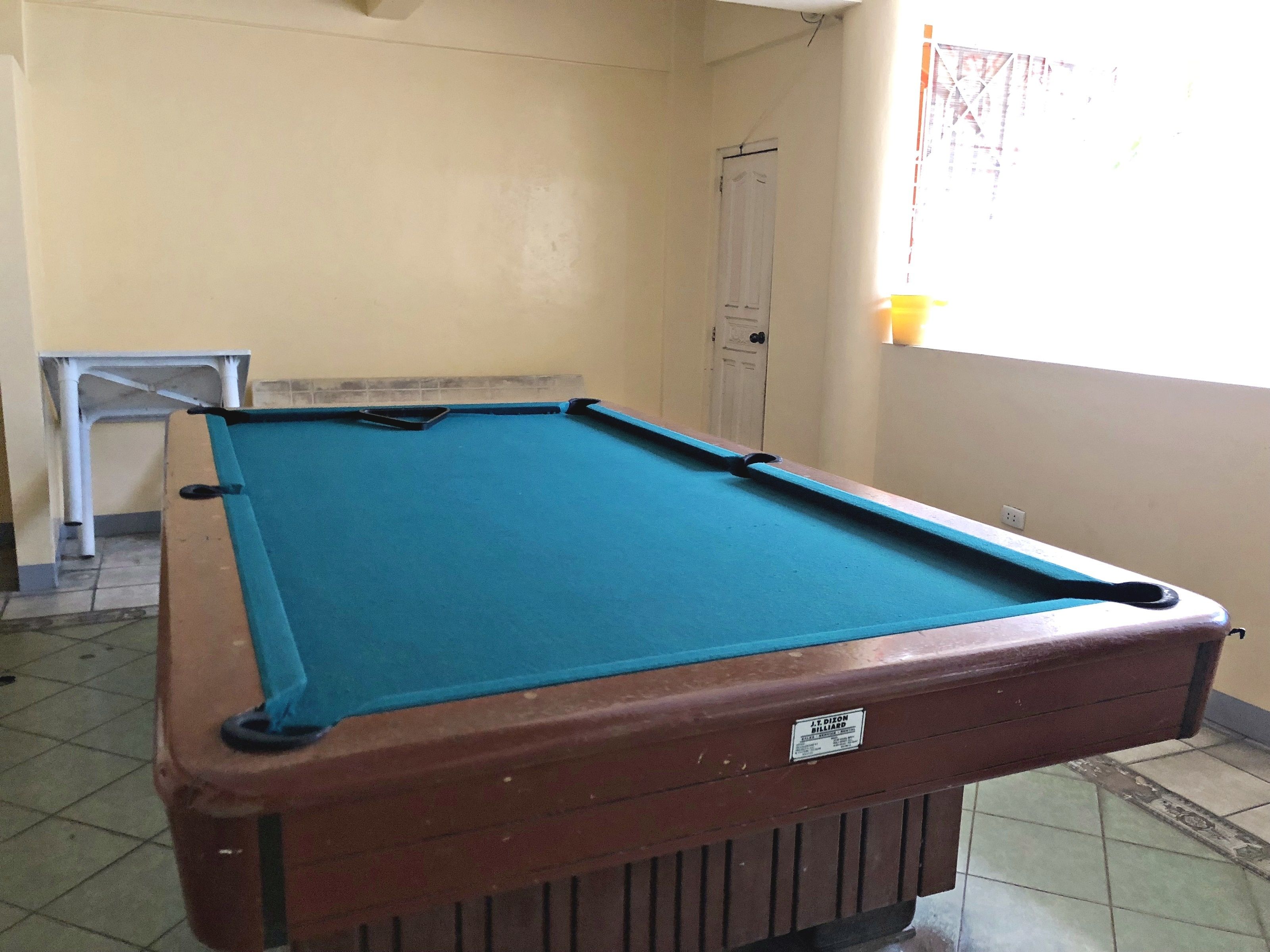 Een pooltafel met een blauwe viltkleed, een bruine tafelbasis en een witte deur op de achtergrond.