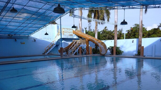 Una piscina interior con tobogán, escaleras y una zona techada con luces colgantes.