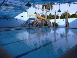 Una piscina interior con tobogán, escaleras y una zona techada con luces colgantes.
