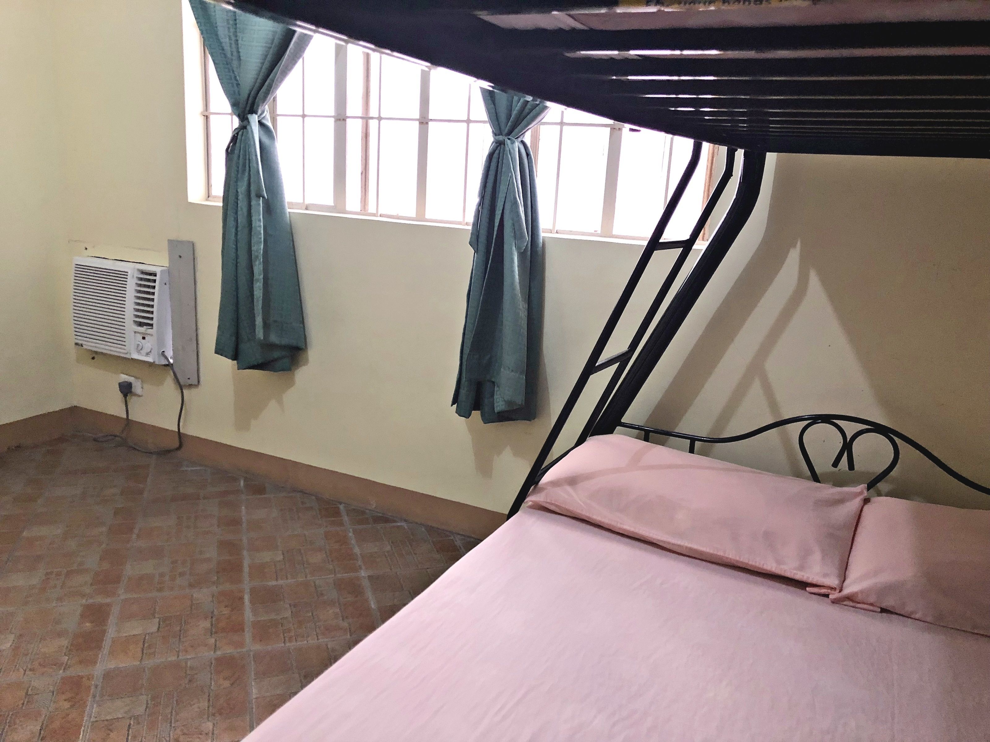 Una habitación con una cama litera, una ventana con cortinas, un calentador de pared y suelo de baldosas.