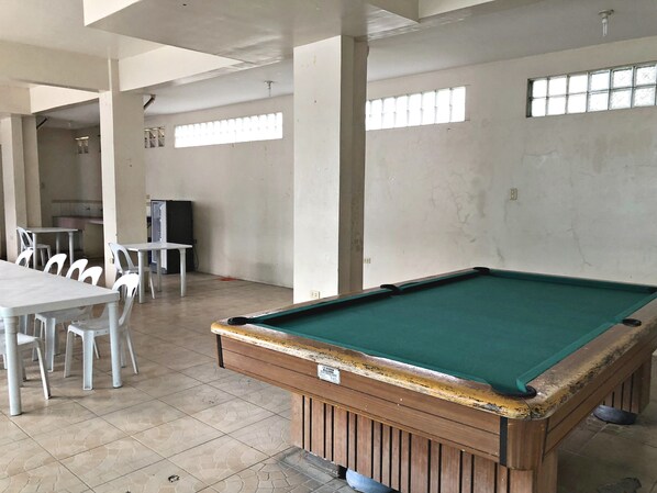 A billiards table in a room with tiled flooring, white chairs, and a television.
