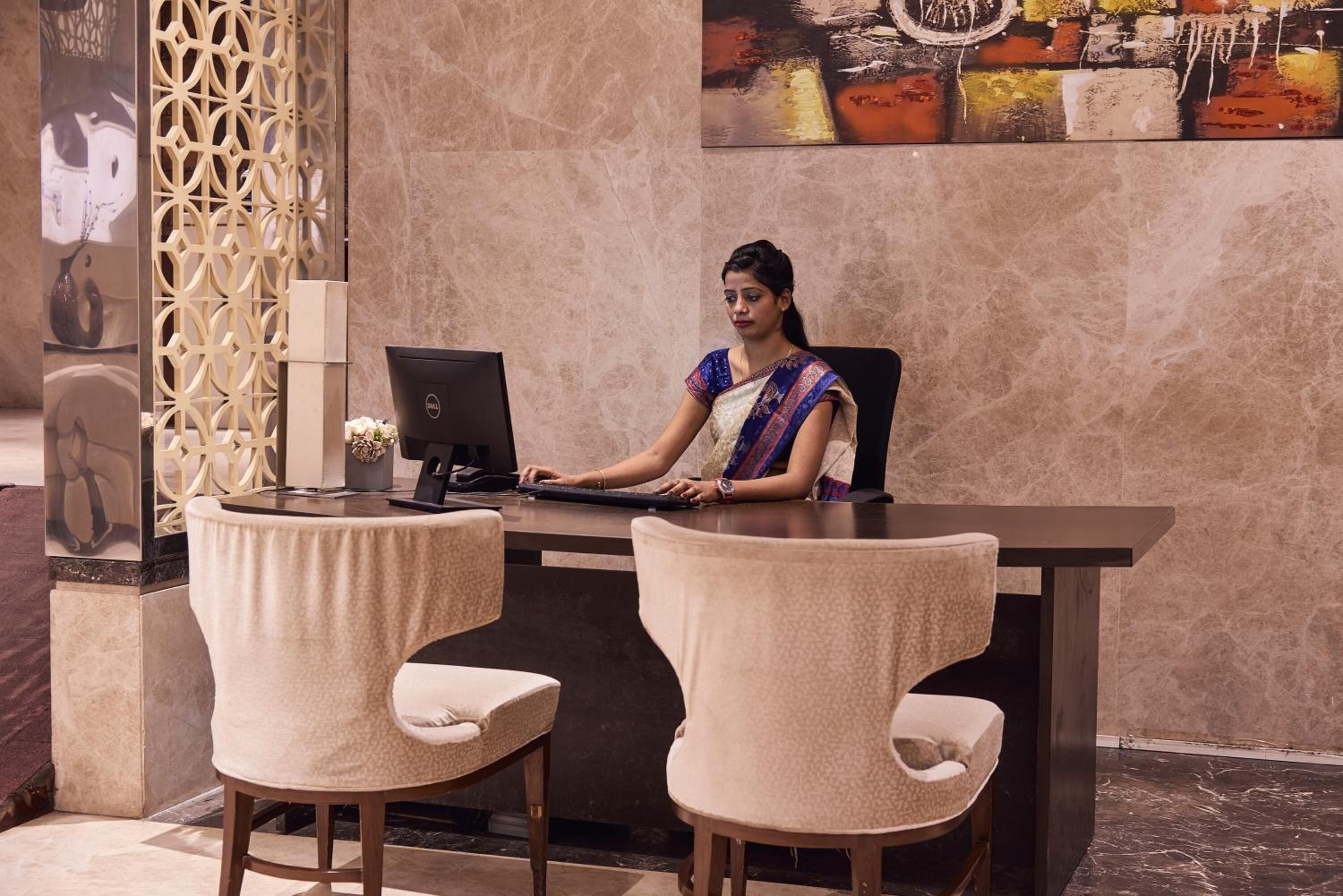 A reception desk with a computer, two cushioned chairs, and a decorative wall panel.