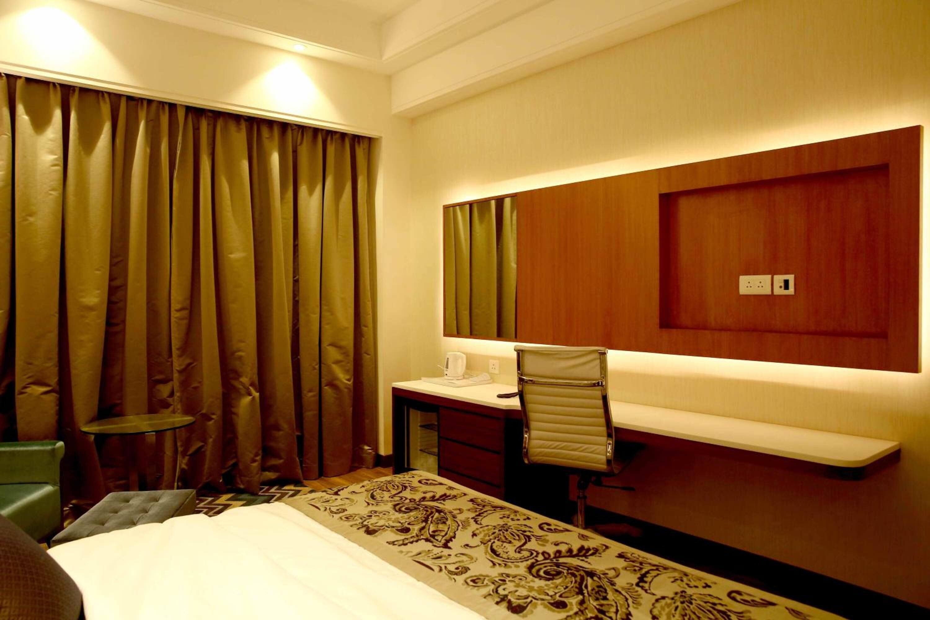 Habitación de hotel con una cama, un escritorio, una silla, una mesita y un espejo.