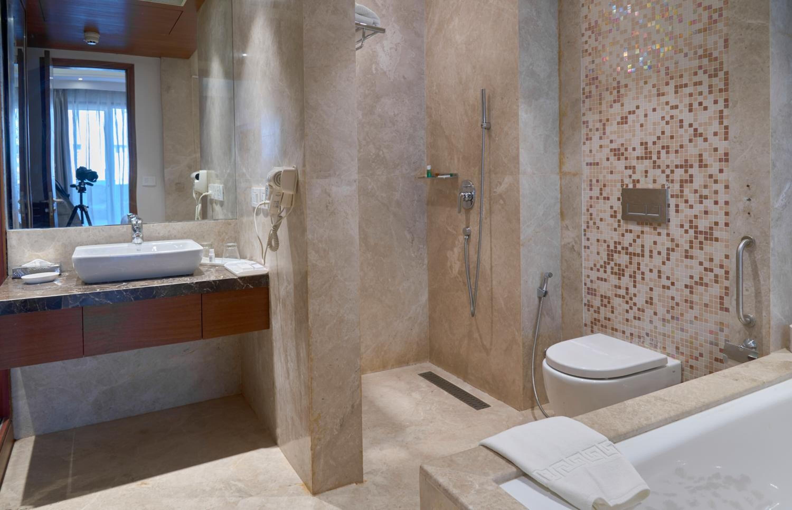 A modern bathroom with a marble sink, a glass shower enclosure, and a mosaic-tiled wall.