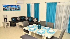 A dining area with a table set for four, a sofa, and curtains. - Departamento vacacional (Playa del Carmen)