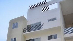 A modern multi-story building with balconies, large windows, and a flat roof. - Departamento vacacional (Playa del Carmen)