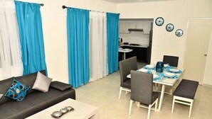 A compact living space with a sofa, coffee table, dining table with chairs, and a kitchenette in the background. - Departamento vacacional (Playa del Carmen)