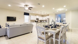 A spacious living area with a sofa, dining table set for six, and a kitchen in the background. - Shv116 - Windsor At Westside #17 - 8 Bed 6 Baths Villa (Kissimmee)