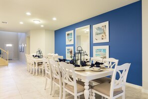 A dining area with white tables and chairs, blue walls, and framed pictures. - Shv116 - Windsor At Westside #17 - 8 Bed 6 Baths Villa (Kissimmee)