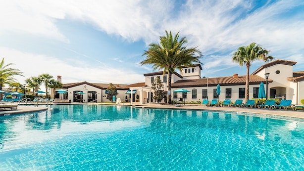 A swimming pool with lounge chairs and palm trees, surrounded by buildings with a Mediterranean architectural style. - Shv116 - Windsor At Westside #17 - 8 Bed 6 Baths Villa (Kissimmee)