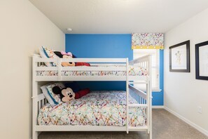 Une chambre avec des lits superposés, un mur d’accent bleu, un doudou à l’effigie de Mickey Mouse et des photos encadrées accrochées au mur.