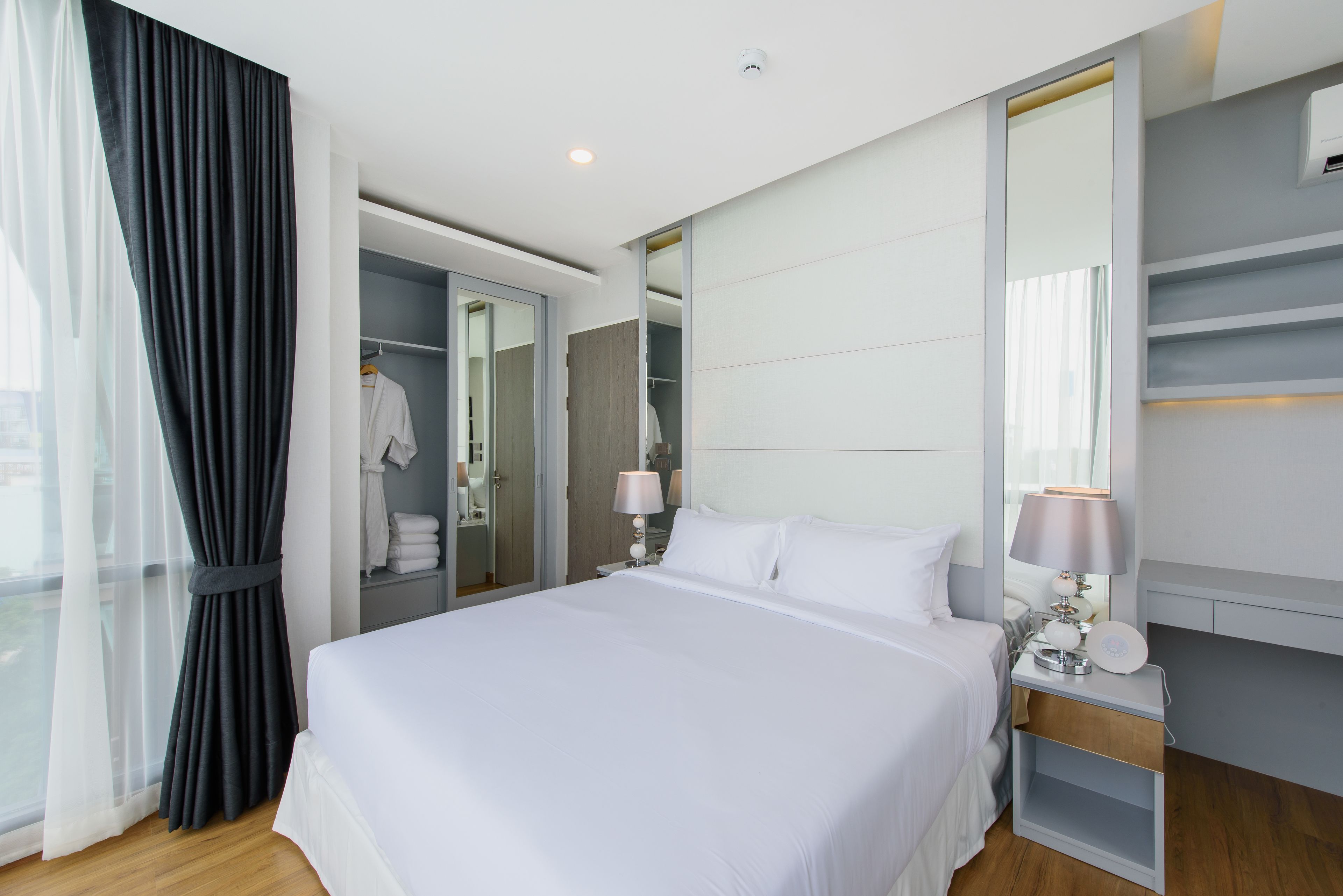 Habitación de hotel moderna con una cama grande, una mesita de noche con lámpara, un armario y un espejo.