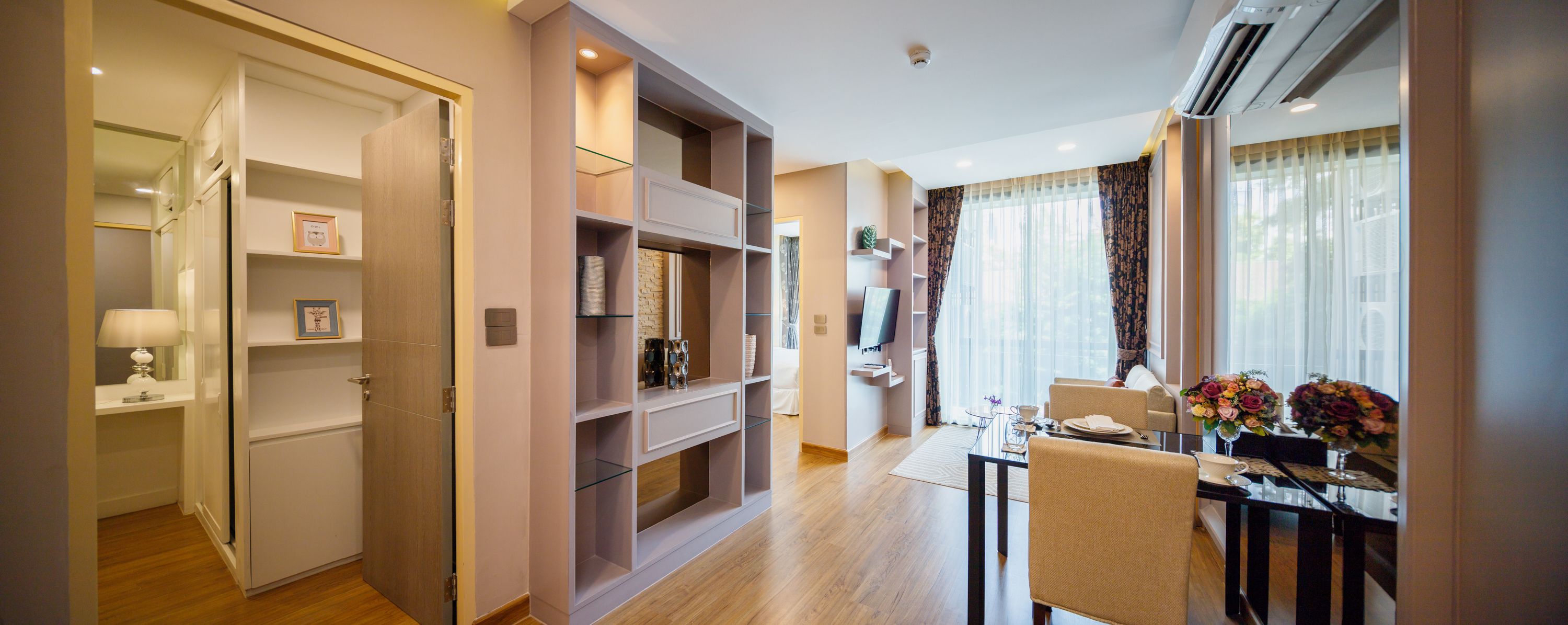 A modern hotel room with a dining area, built-in shelving, and a TV.