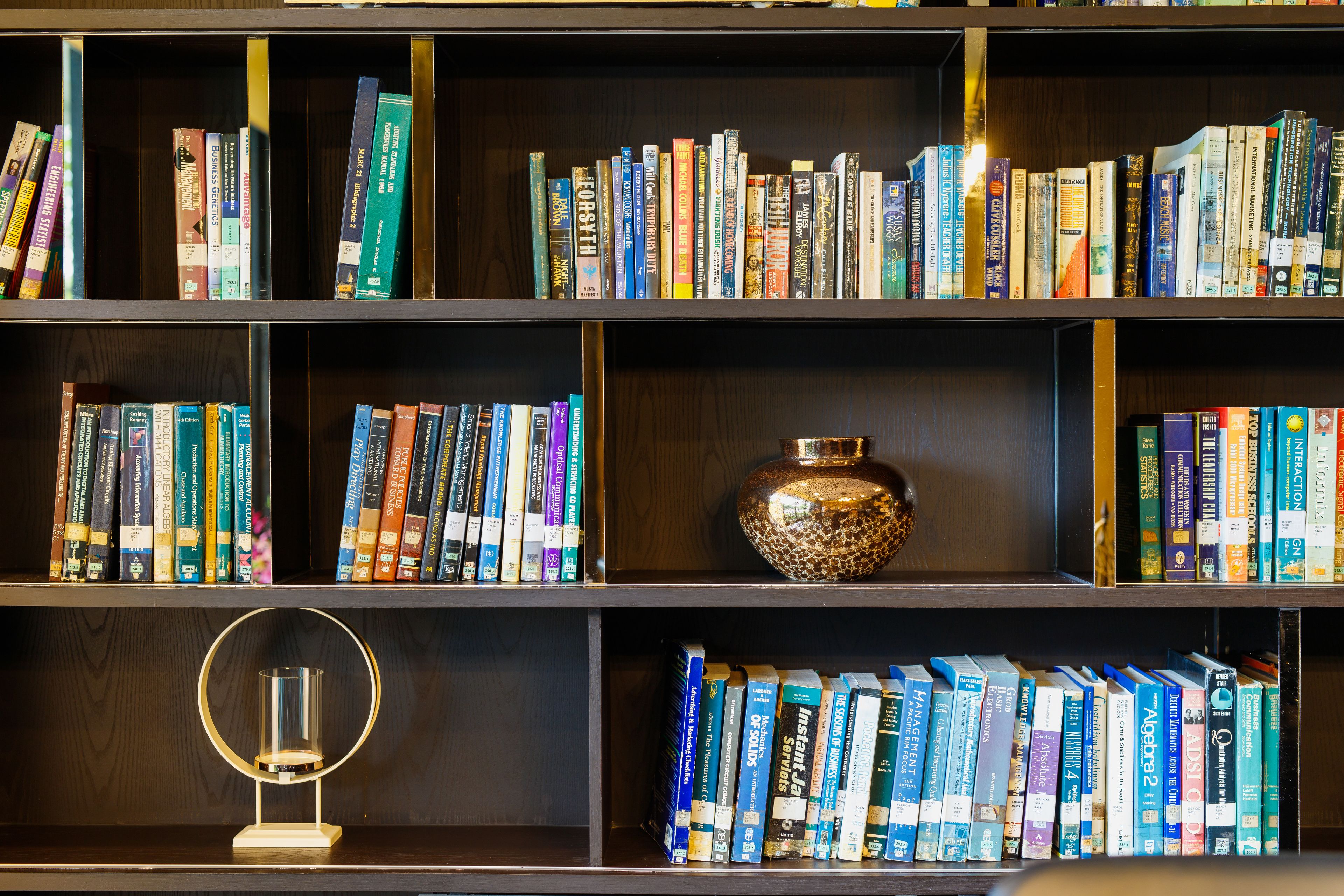 Una estantería con varios libros y un jarrón decorativo.