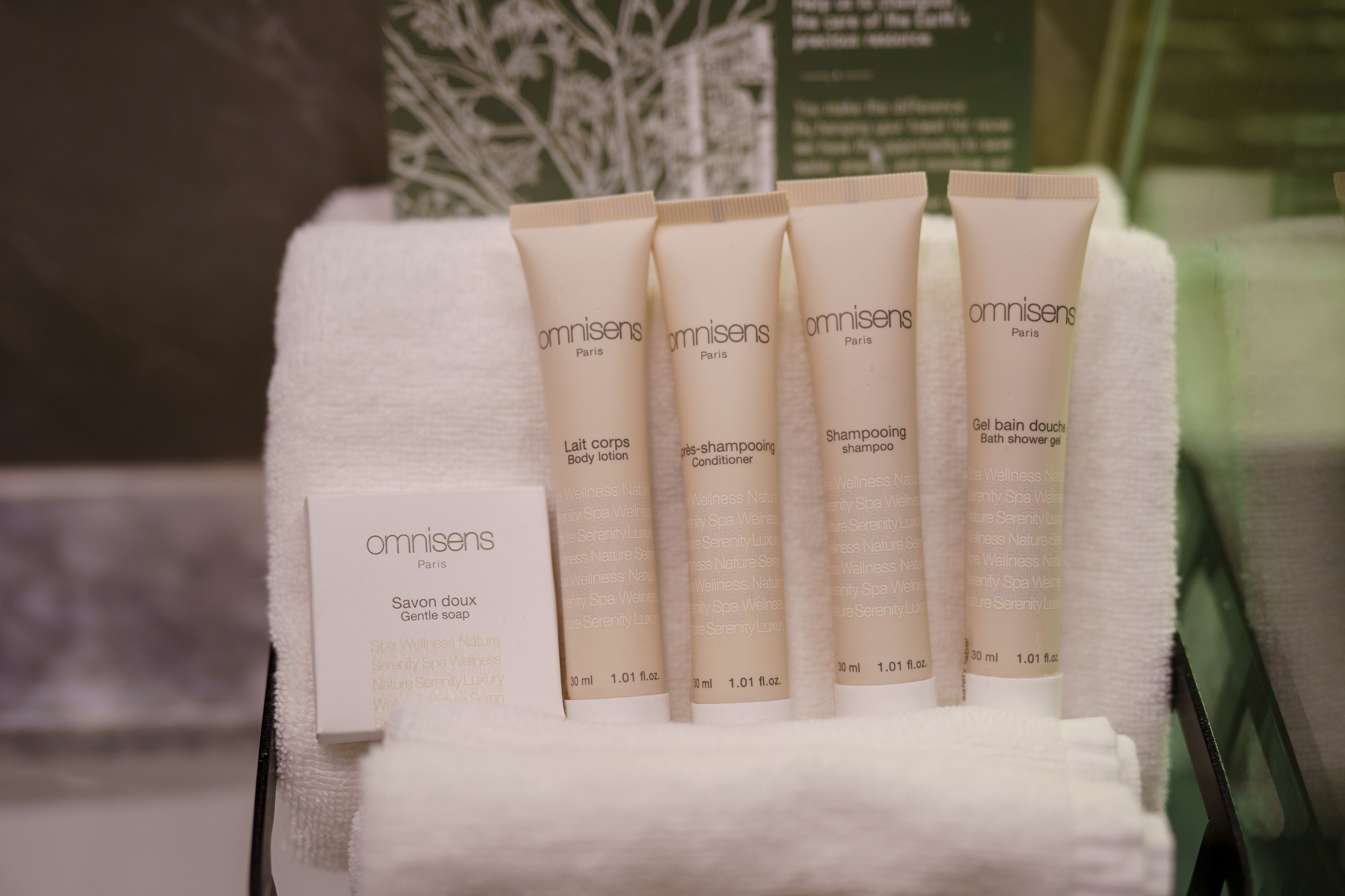 Presentatie van Omnisens Paris spa producten, waaronder body lotion, shampoo, conditioner en douchegel, uitgestald op een witte handdoek.