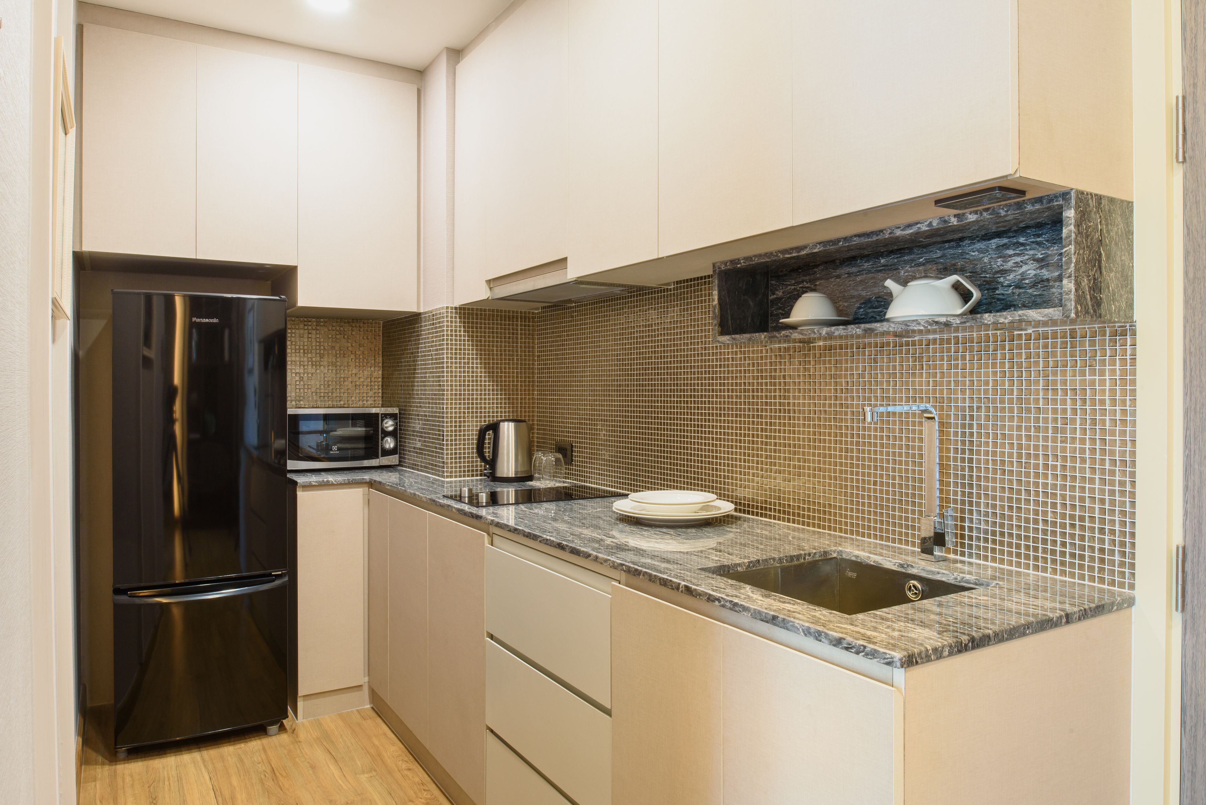 Una cocina compacta con un refrigerador de acero inoxidable, un microondas, un lavamanos y un salpicadero azulejado.