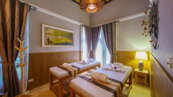 A hotel room with two beds, a painting on the wall, a wooden bench, a standing lamp, and a window with curtains.