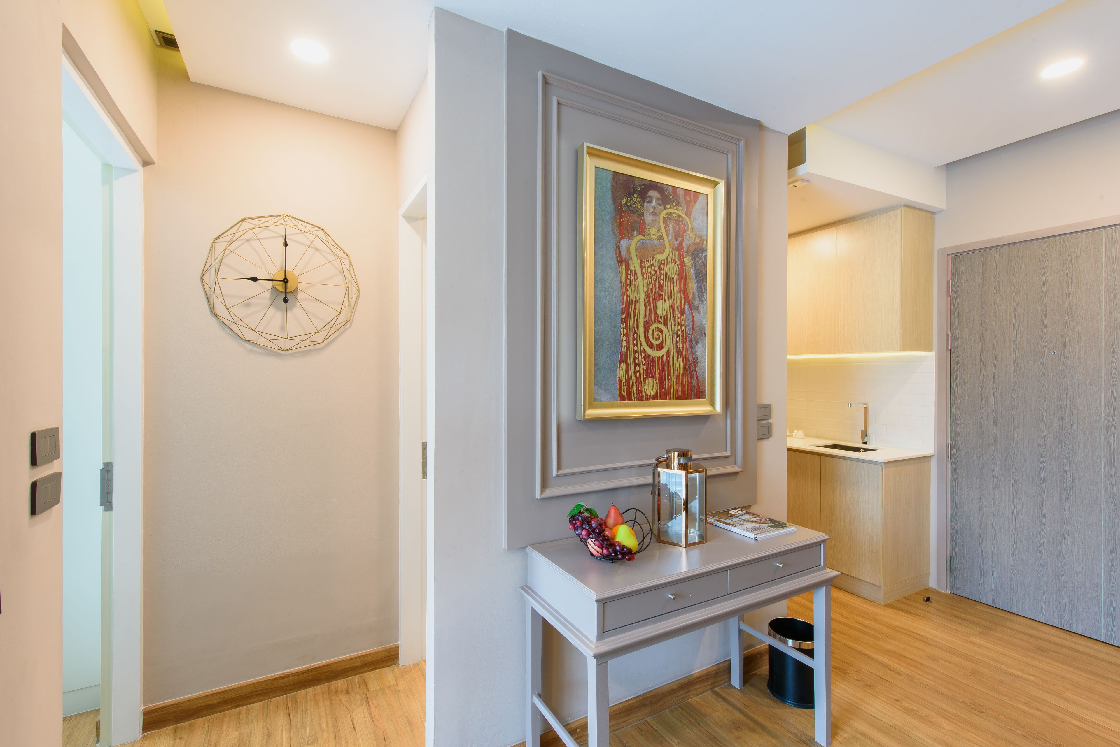 Un intérieur moderne avec un bureau, une œuvre d’art encadrée, une horloge aux motifs géométriques et un espace cuisine minimaliste.