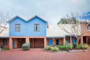 Una hilera de casas azules con cimientos de ladrillo, un sendero pavimentado y jardines.