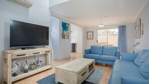 Una sala de estar con televisor de pantalla plana, mueble de madera para equipo multimedia, sofá azul y una mesa de centro de madera.