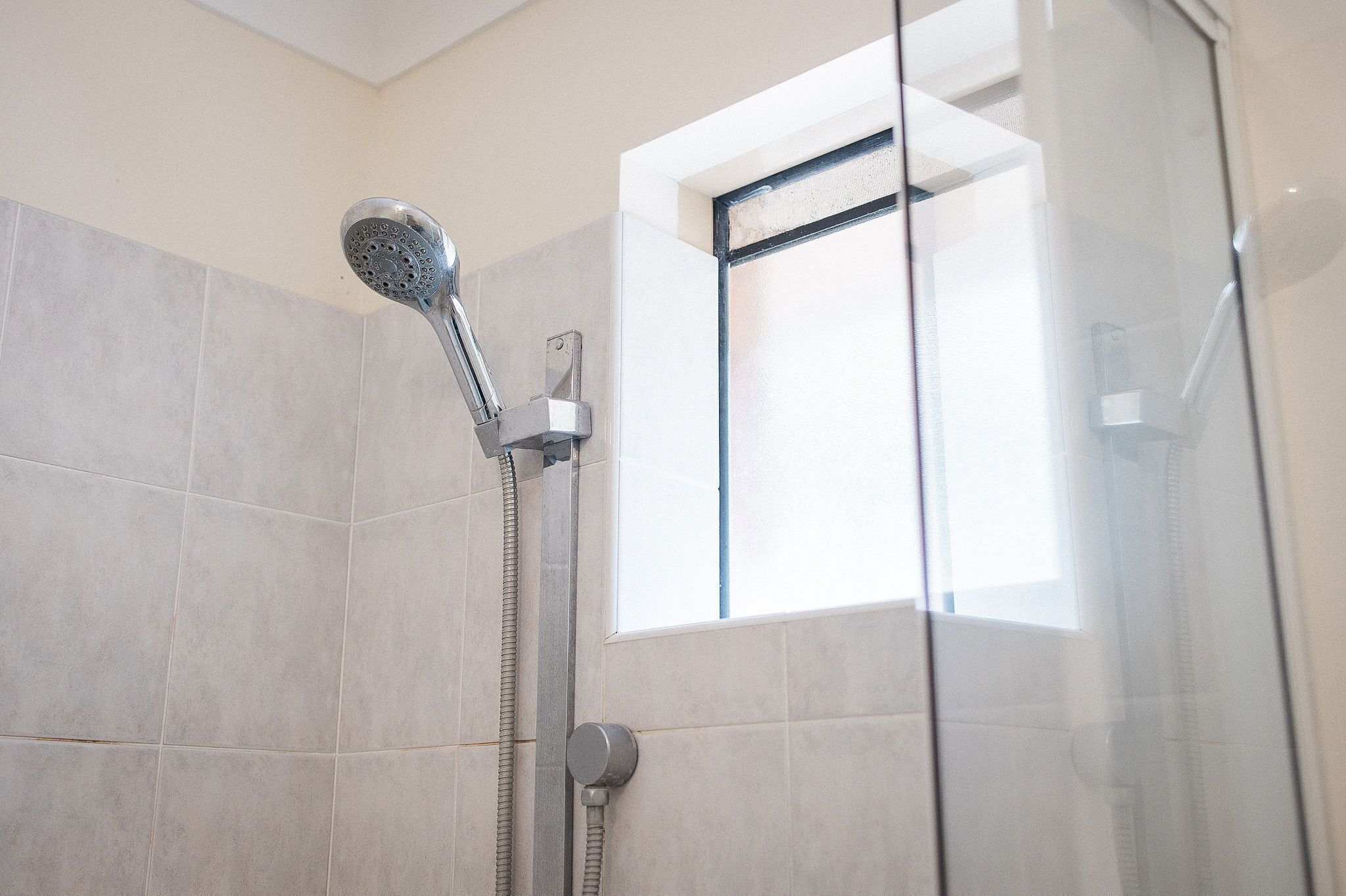 A shower with a handheld showerhead and a wall-mounted control.