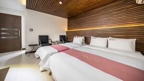 A hotel room with two beds, a wooden ceiling, a desk with a chair, and a minibar. - Q Hotel (Paju)
