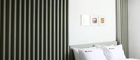 Habitación de hotel con pared a rayas, cama con ropa blanca, mesita de noche con teléfono y pañuelos, y una silla.