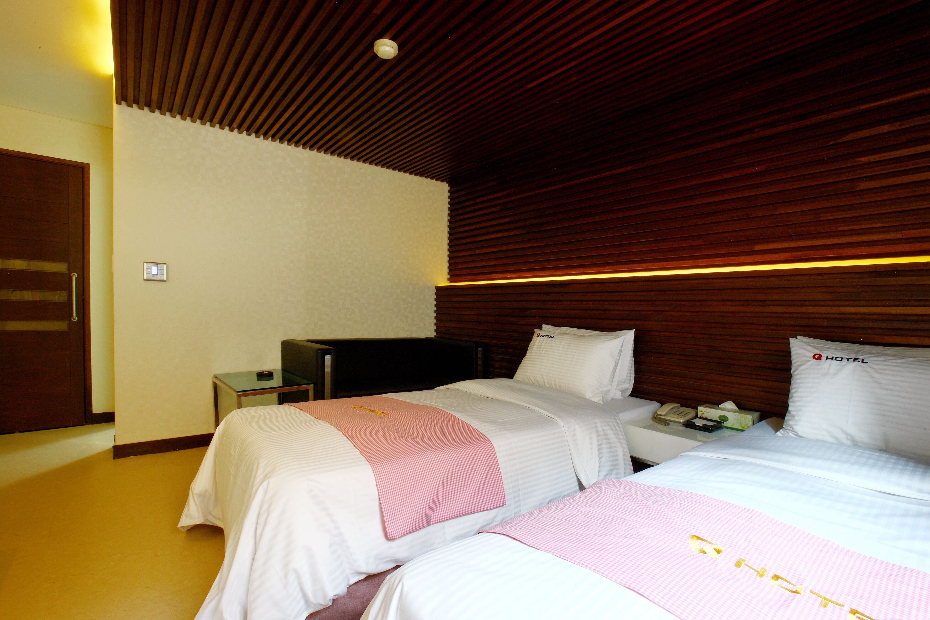 Una habitación de hotel con dos camas, techo de madera, mesita de noche con teléfono y una puerta.