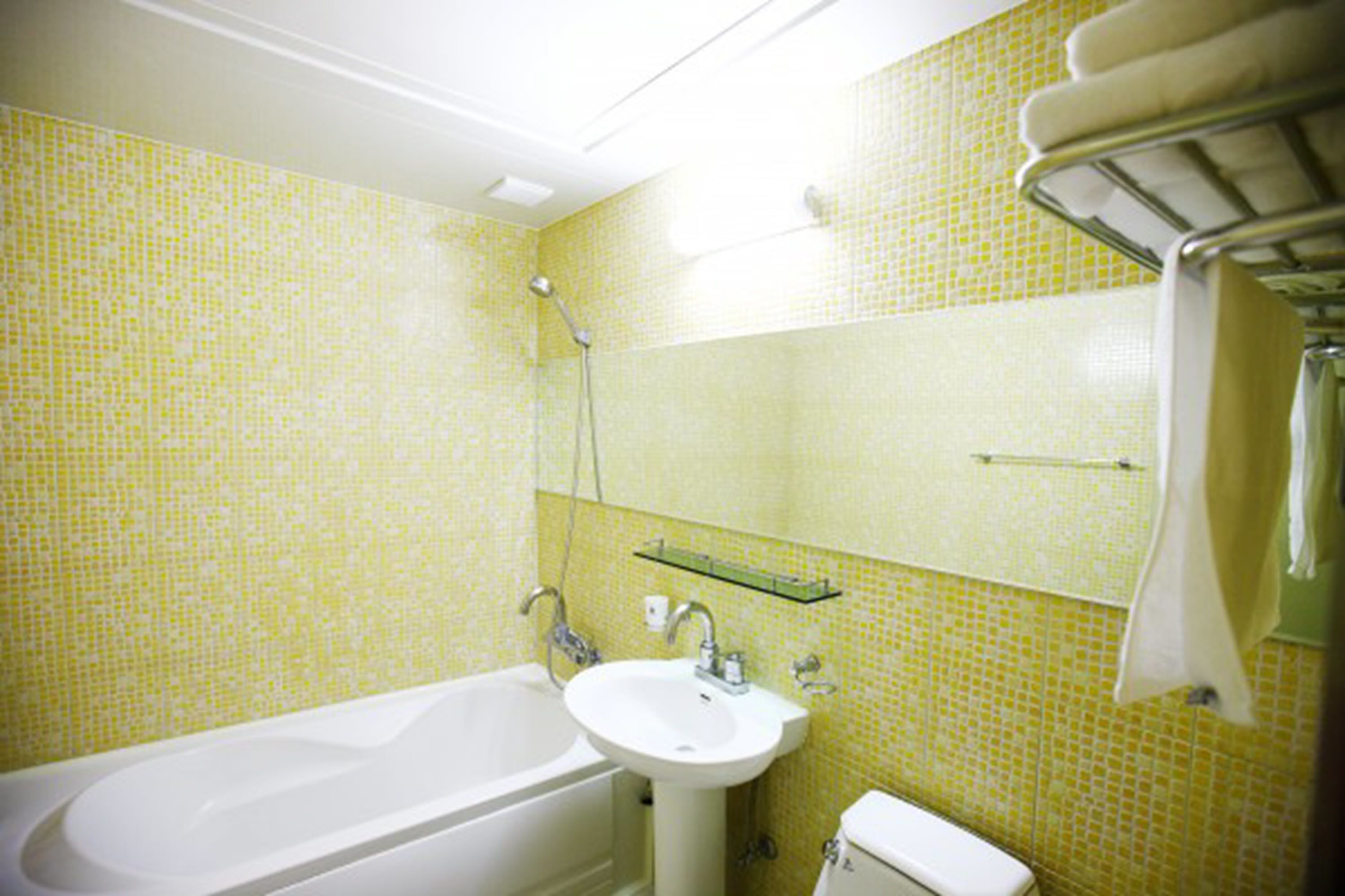 A bathroom with a bathtub, sink, and toilet. There is a mirror above the sink and a towel rack on the wall.
