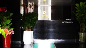 A reception area with a glass-tiled floor leading to a reception desk. There are potted plants on either side of the reception desk. - Q Hotel (Paju)
