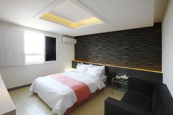 A modern hotel room with a bed, a small bedside table, a black sofa, and a unique ceiling design.