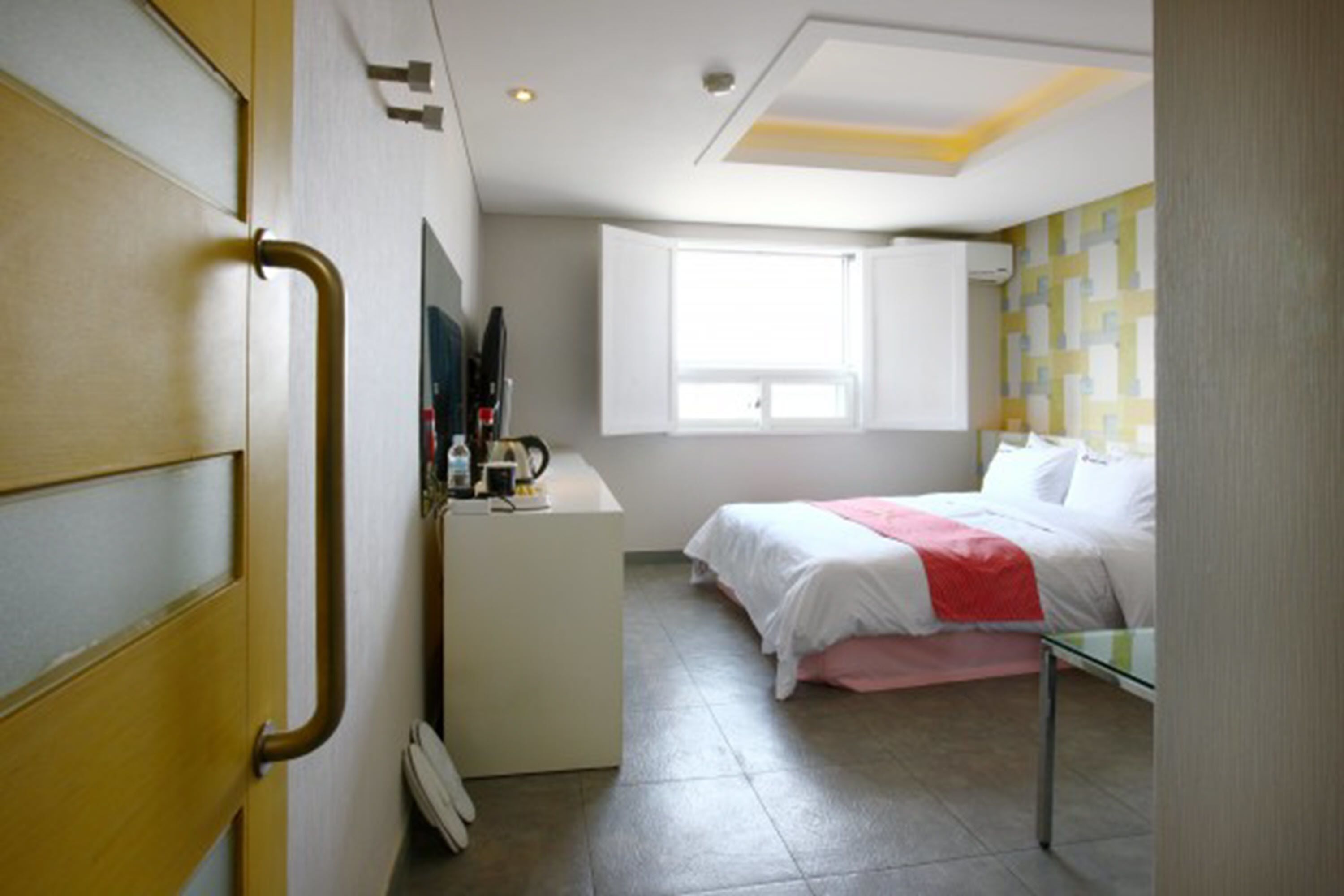 A hotel room with a bed, a desk, a chair, a window, and a door.