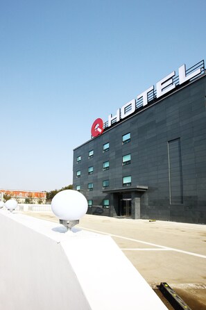 A modern hotel building with a prominent red logo on the roof and a flat facade.