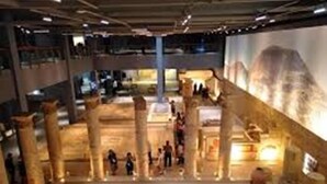 An interior view of a museum with ancient columns, a central mosaic floor, and visitors. - Yilmazel Hotel (Gaziantep)