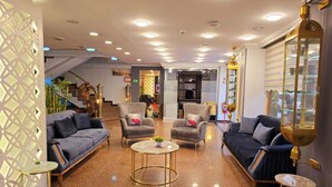 Un hall d’entrée spacieux avec un plafond haut, plusieurs coins salon et une table basse centrale.