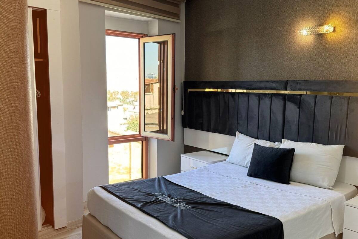 A bedroom with a large bed, a nightstand, a wardrobe, and a window with a view.