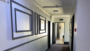 Un couloir doté d’un sol recouvert de moquette, de murs blancs et de cadres de tableaux noirs.