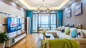 A modern living room with a flat-screen TV, a sofa, a coffee table, and a large window with curtains. - Enjoy Stay YUNWEI Apartment (Chengdu)