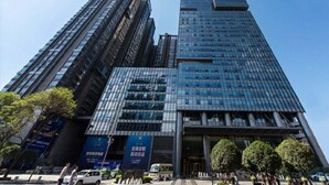 A modern high-rise building with a glass facade, featuring a prominent entrance and surrounding greenery. - Enjoy Stay YUNWEI Apartment (Chengdu)