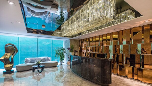 A modern lobby with a curved reception desk, a seating area with a sofa and coffee table, and a large glass wall reflecting the interior. - Enjoy Stay YUNWEI Apartment (Chengdu)