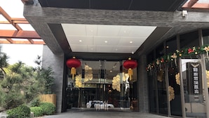 A modern building entrance with glass doors, decorative lanterns, and a well-maintained garden area. - Yidear Hotel (New Taipei City)