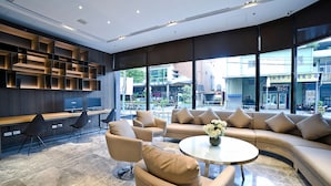 A modern lobby with a curved sofa, a round coffee table, and a TV. - Yidear Hotel (New Taipei City)