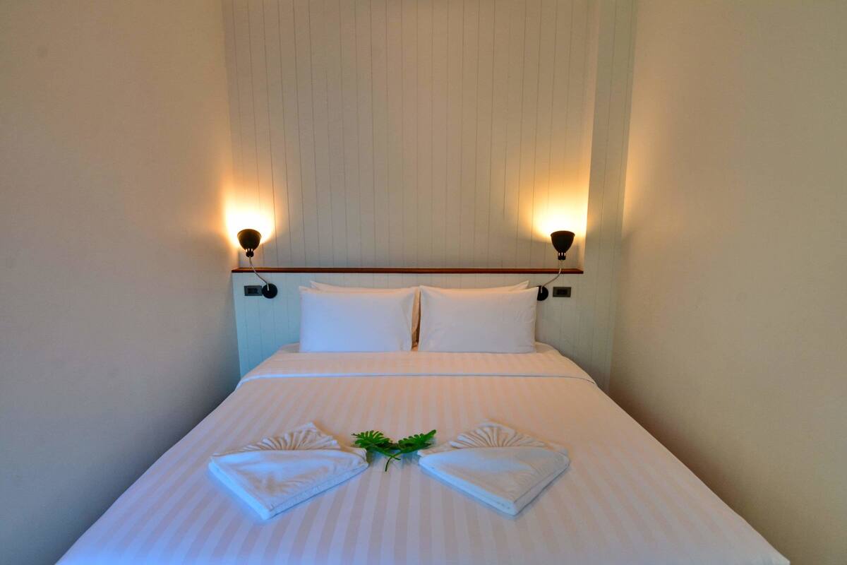 A neatly made bed with white linens and two pillows, flanked by wall-mounted lamps.
