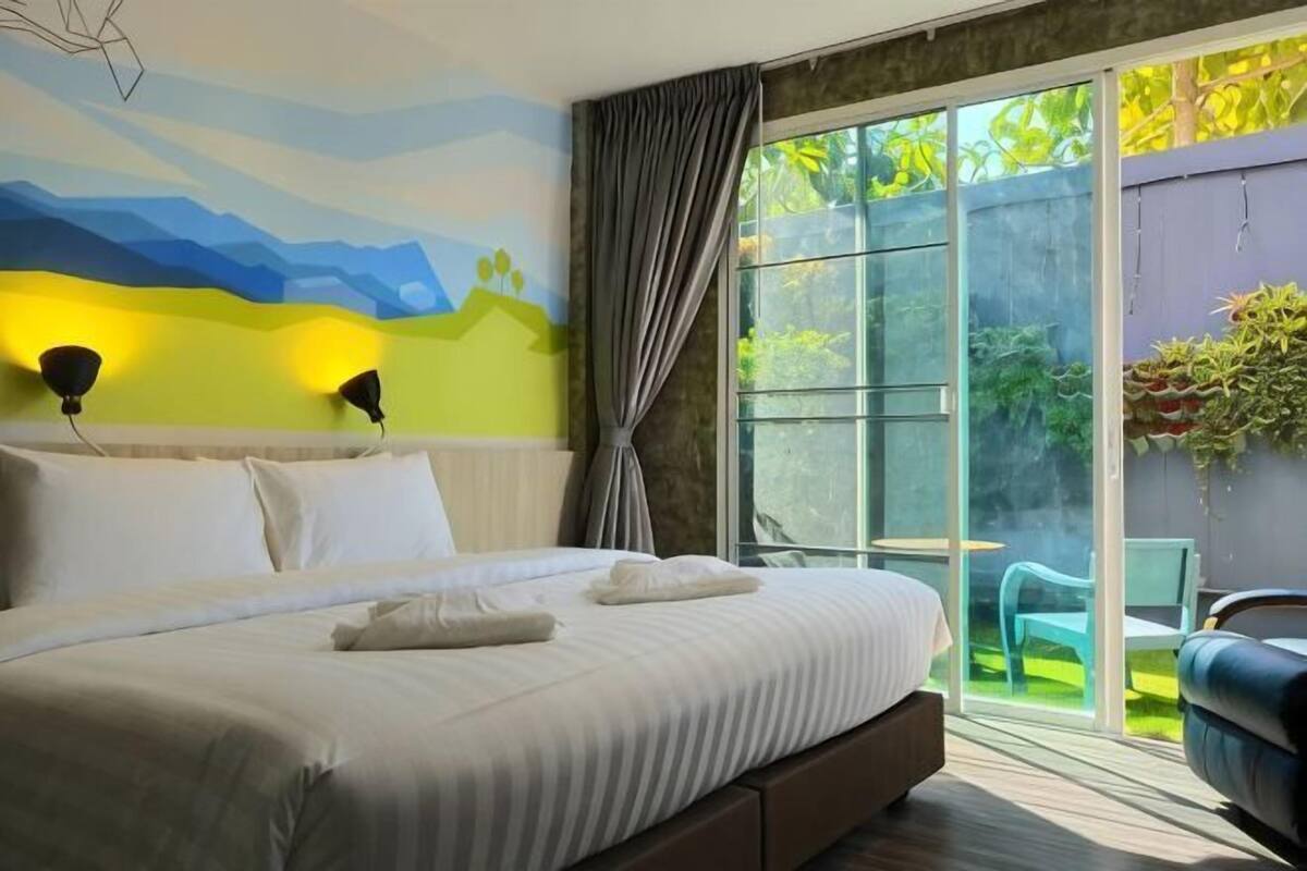 A bedroom with a large bed, a sliding glass door to a balcony, and a view of greenery.
