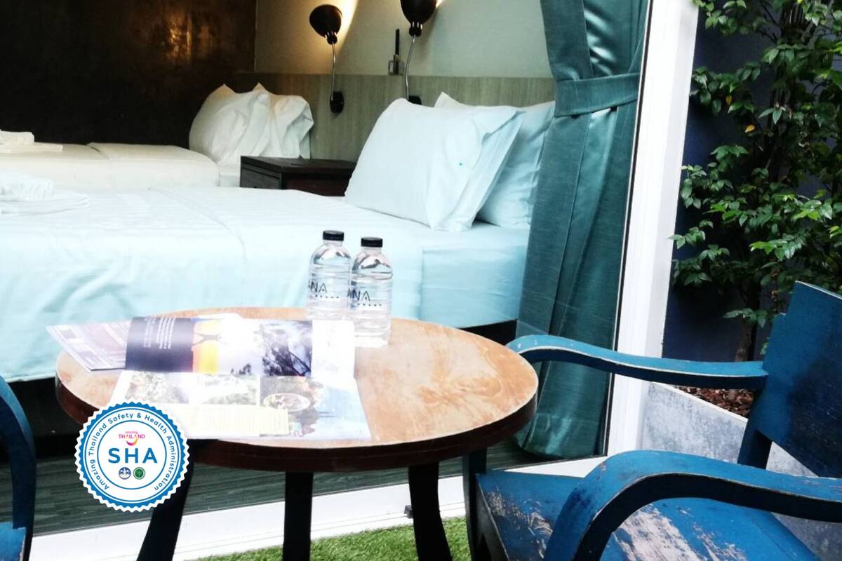 A hotel room with two beds, a table with water bottles, and a view of greenery outside.