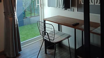 Una habitación con un escritorio de madera, una silla, un televisor y vistas a un jardín a través de un ventanal.